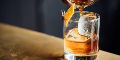 Amber whiskey pouring through a strainer into a glass with a large ice cube