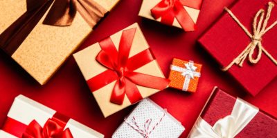 Assorted gift boxes in kraft, red and white, tied with ribbon bows, arranged on a red surface
