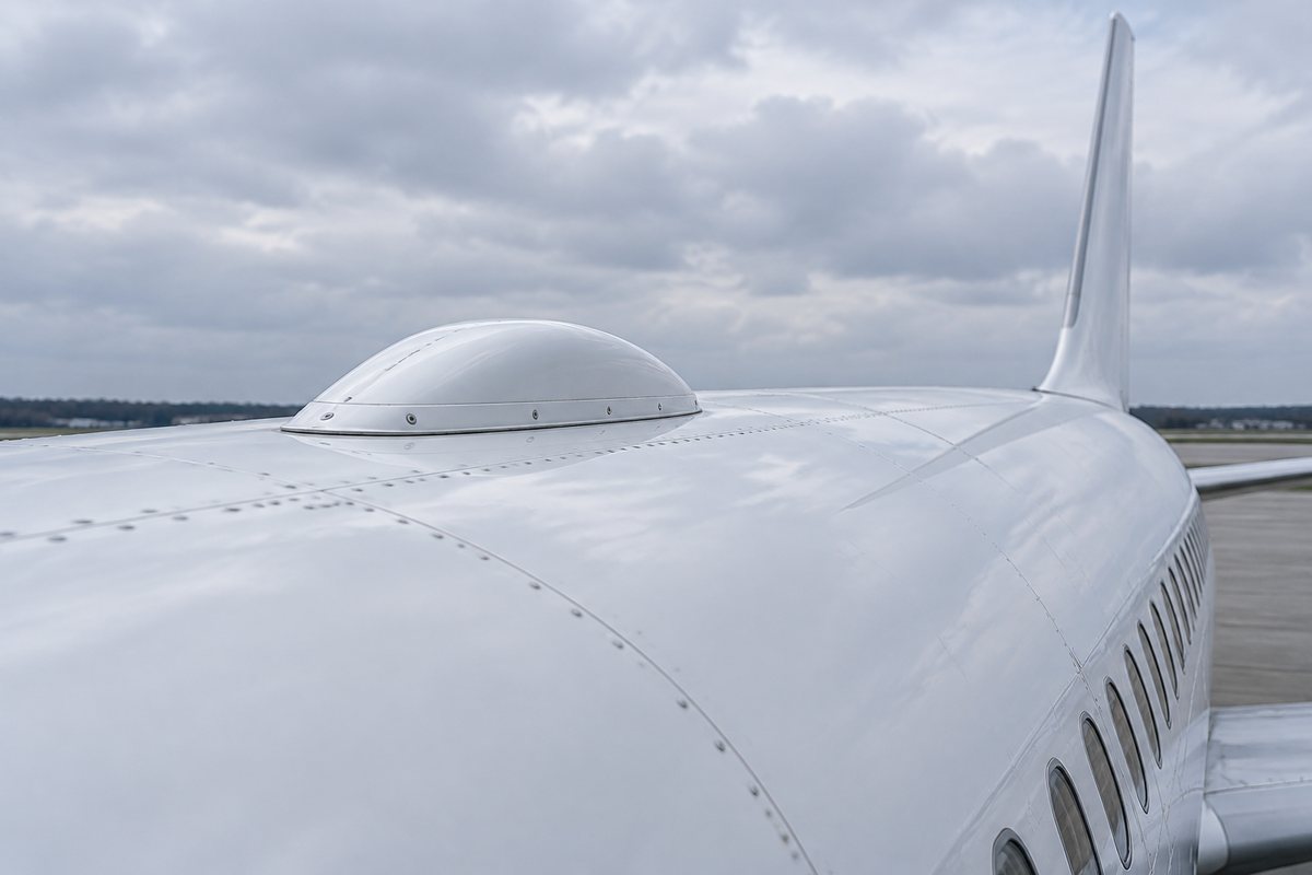 The low dome of a satellite antenna on top of a plain white airliner fuselage