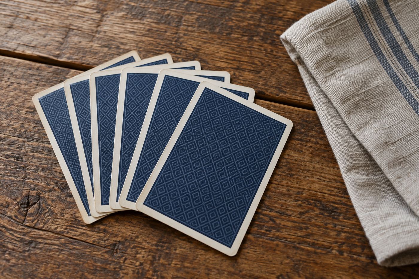 A fan of face-down playing cards beside folded linen on a wood table.